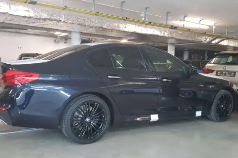 Ciemnogranatowe BMW 520d xDrive z czarnymi felgami stoi w garażu.