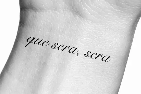 Tatuaż na nadgarstku z napisem "que sera, sera", co oznacza "co ma być, będzie".
