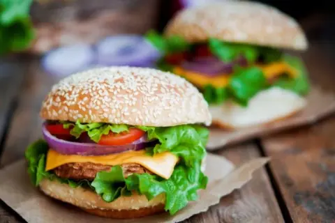 Dwa soczyste burgery z domowym fast foodem, pełne świeżych warzyw i sera, na drewnianym stole.