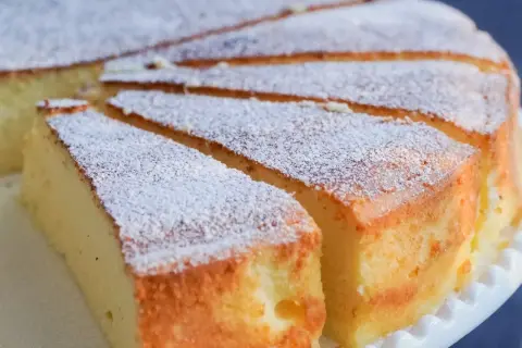 Pokrojony sernik posypany cukrem pudrem na białym talerzyku.