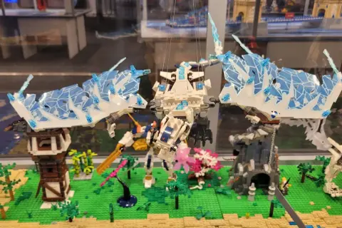 Lodowy smok w muzeum LEGO w Warszawie walczy z robotem na tle miniaturowej wioski.