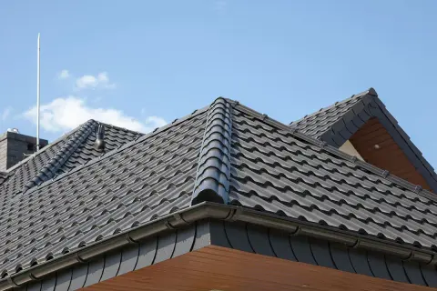 Szary dach czterospadowy z dachówki ceramicznej, z widocznym kominem i piorunochronem.