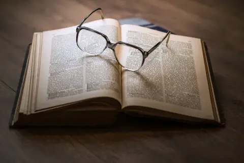 Eine Brille liegt auf einem aufgeschlagenen Buch mit informierenden Texten.