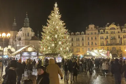 Ein festlich beleuchteter Weihnachtsbaum auf dem Prager Weihnachtsmarkt, umgeben von Buden und Menschen.