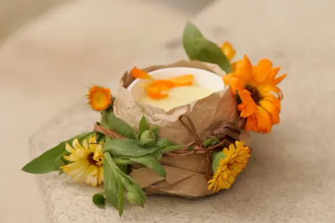 Selbstgemachte Ringelblumensalbe in einem Becher, verziert mit frischen Ringelblumen und Blättern.