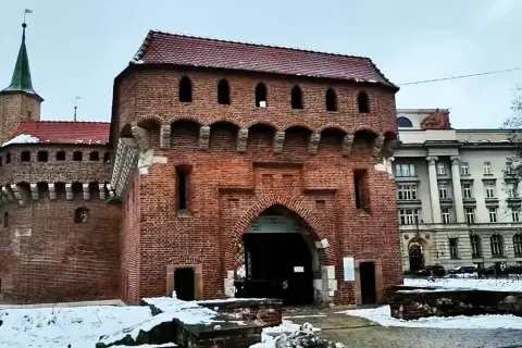 Imponujący barbakan kraków z cegły, z charakterystycznymi łukami i blankami, otoczony zimowym krajobrazem.