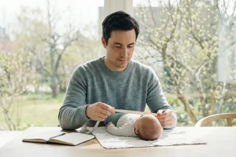 Pappa mäter sin bebis för 10 månaders kontroll bvc. En lugn stund vid fönstret.