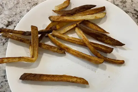 En tallrik med krispiga pommes frites, perfekt tillagade i airfryer. Saltkorn glittrar på de gyllene pommes.
