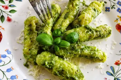 Pyszne gnocchi z pesto, posypane parmezanem i udekorowane listkami bazylii. Widok na talerzu z kolorowym wzorem.