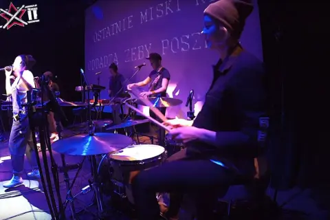 Wiktoria Jakubowska na perkusji, w rytmie muzyki, z pałeczkami w dłoniach, tworzy energię na scenie.