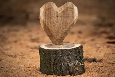 Holzskulptur in Herzform auf einem Baumstumpf, umgeben von Holzspänen.