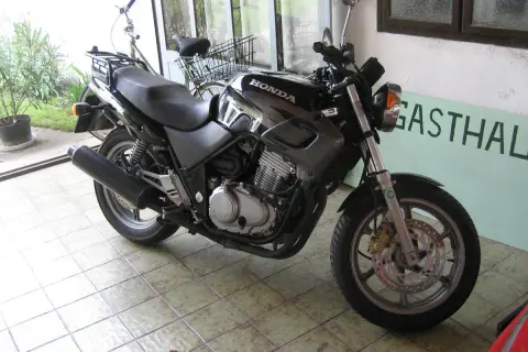 Czarny motocykl Honda z widocznym silnikiem i wydechem, gotowy do jazdy. Obok stoi rower.