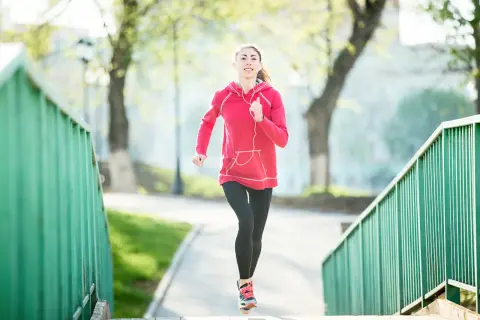 Une jeune femme en tenue de sport court sur un chemin bordé de verdure. Elle semble apprécier son activité, peut-être pour courir 20 minutes par jour.