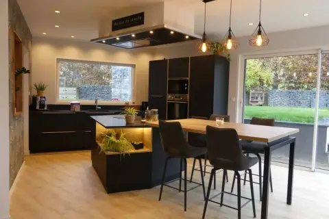 Cuisine moderne avec îlot central, plan de travail noir et carrelage marron foncé. Table haute avec tabourets, luminaire design.