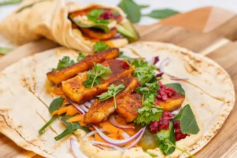 En läcker halloumi wrap med hummus, rivna morötter, rödlök och färska örter. En annan wrap syns i bakgrunden.