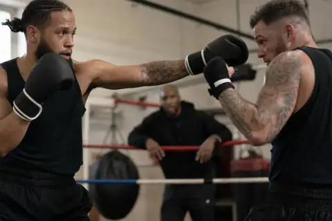 Two boxers spar in a ring, one throwing a jab, demonstrating how to counter punch. A coach watches from the background.
