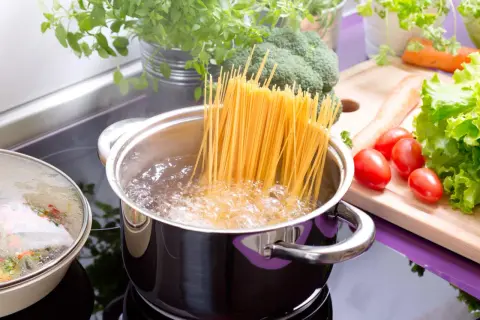 Spaghetti kochen in sprudelndem Wasser. Frisches Gemüse wie Brokkoli, Karotten und Tomaten liegen bereit für eine gesunde Mahlzeit.