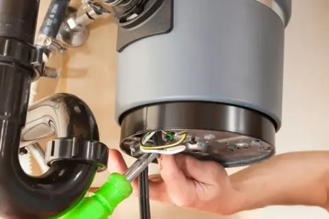 A person is working on a garbage disposal that is not working, connecting wires with a screwdriver.