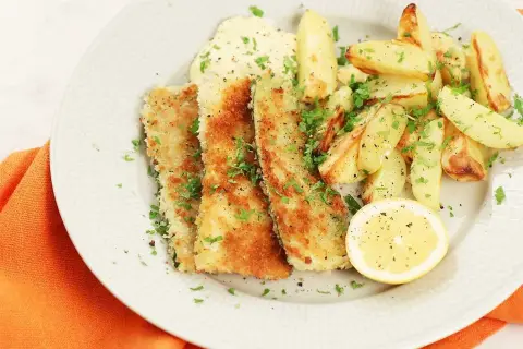 Krispiga bitar av pankopanerad zucchini serveras med ugnsrostade potatisklyftor, en klick sås och en citronskiva.