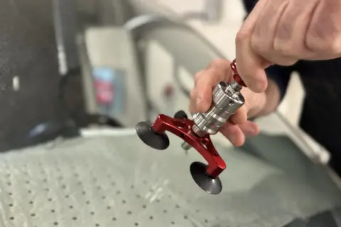 En person använder ett verktyg för att laga en spricka i en bilruta. Verktyget har sugproppar och en metallkonstruktion.