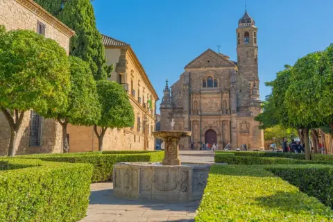 Fuente renacentista en plaza de Úbeda y Baeza, con iglesia barroca al fondo y árboles frutales.