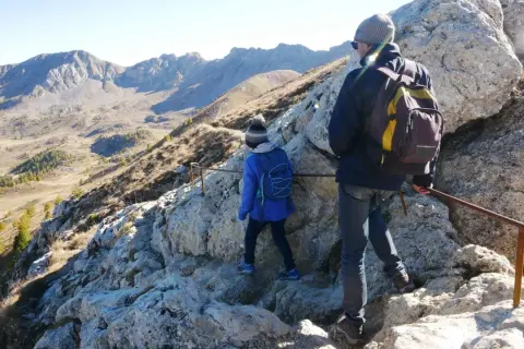 Deux randonneurs escaladent un sentier rocheux près du pic de Morgon, profitant d'une vue imprenable sur les montagnes.