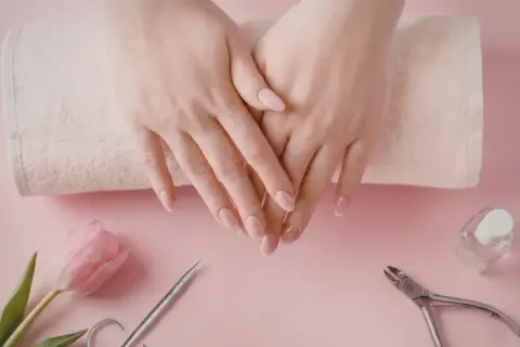Delikatne dłonie z perfekcyjnym manicurem kombinowanym, obok różowy tulipan, cążki i buteleczka lakieru.