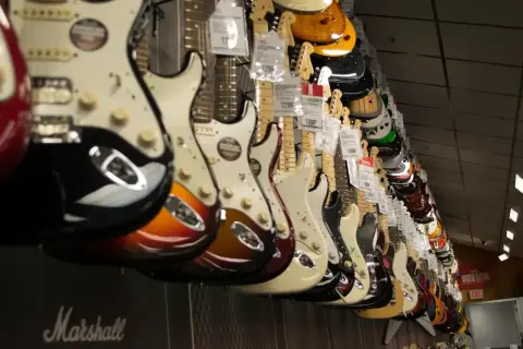 Rząd gitar elektrycznych w sklepie. Widać różne kolory i modele, w tym pierwsza gitara elektryczna z pięknym wykończeniem.