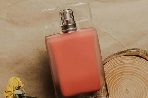 Perfumy Lancome Oui w koralowym odcieniu, obok suszonej róży i plastra drewna.