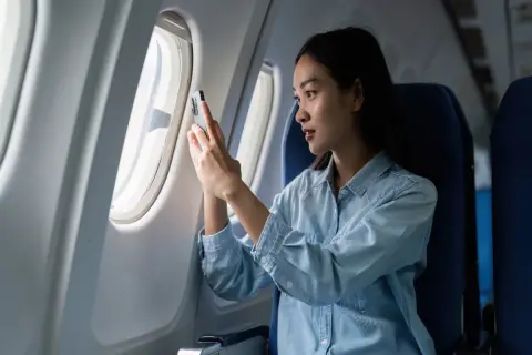 Kobieta w samolocie sprawdza telefon, zastanawiając się, czy w samolocie jest internet.