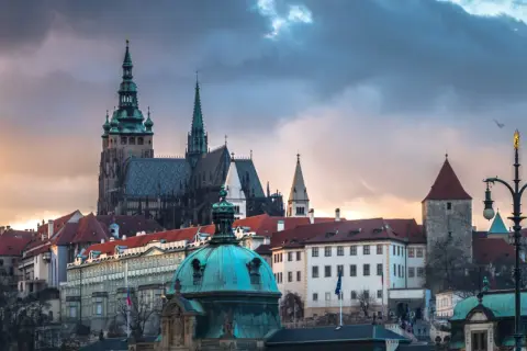 Prag dom mit seinen Türmen und Dächern unter dramatischem Himmel. Ein Vogel fliegt über die historische Kulisse.