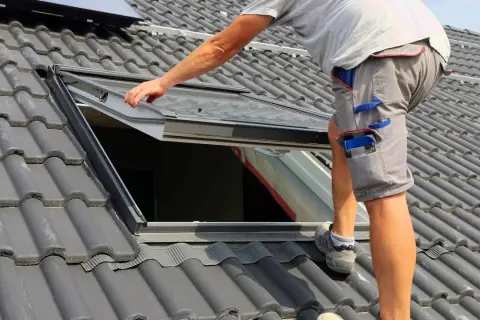 Pracownik montuje okno dachowe. Zastanawiasz się, ile kosztuje okno dachowe? Sprawdź ceny!