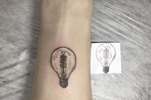 Nowy tatuaż żarówka na skórze, obok szkicu. Symbol pomysłu i światła.