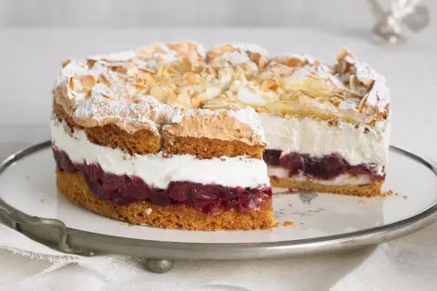 Eine köstliche Hansen Jensen Torte mit Kirschen, Sahne und Baiserhaube, bestreut mit Mandelblättchen und Puderzucker.