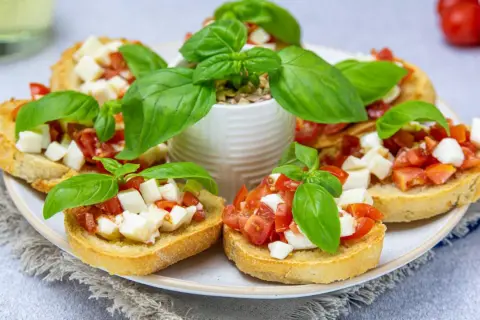 Przepis na bruschettę z pomidorami i mozzarellą: chrupiące grzanki z soczystymi pomidorami i kremową mozzarellą, ozdobione świeżą bazylią.