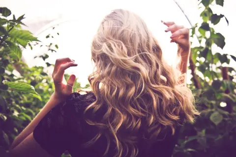 Frau mit welligem, blondem Haar, das durch Reverse Balayage einen natürlichen Farbverlauf erhält. Vorher-Nachher-Effekt im Grünen.