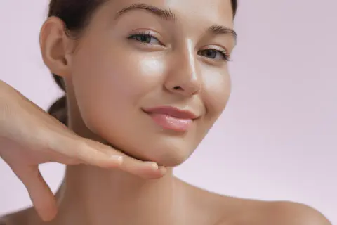 Strahlendes Gesicht einer Frau, die ihr Kinn berührt. Die Haut wirkt glatt und jugendlich, ein Zeichen für die positive retinol wirkung.