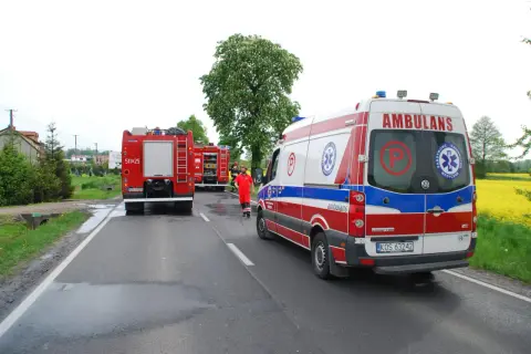 Strażacki bosak leży na drodze obok wozu strażackiego i karetki pogotowia.