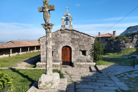 Crucero y ermita de piedra en el Castro de Santa Trega, bajo un cielo azul.