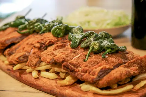 Un festín de cachopo crujiente, patatas fritas doradas y pimientos de Padrón. ¡Una delicia para compartir!