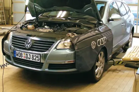 Passat B6 2.0 TDI 140KM w warsztacie, z otwartą maską i osłoną na błotniku. Obok klawiatura i myszka.