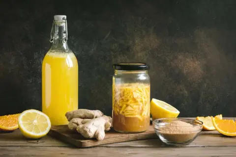 Zutaten für ingwer fermentieren: frischer Ingwer, Zitronen, Orangen und Zucker. Daneben eine Flasche mit gelbem Getränk.