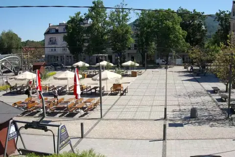 Letni dzień na rynku w Ustroniu. Puste stoliki kawiarniane czekają na gości, a słońce rzuca cienie na brukowany plac.