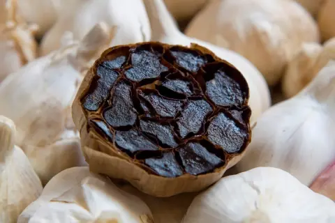 Gousse d'ail noir coupée, révélant ses gousses sombres et moelleuses, entourée d'ail blanc frais. L'ail noir bienfaits et méfaits intriguent.