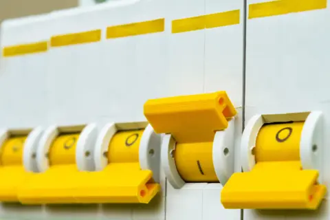 Rząd żółtych wyłączników automatycznych, pokazujący różne rodzaje bezpieczników.