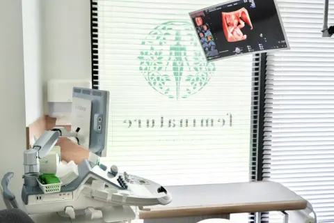 Gabinet ginekologiczny na NFZ w Warszawie. Aparatura USG z obrazem płodu, sprzęt medyczny i leżanka.