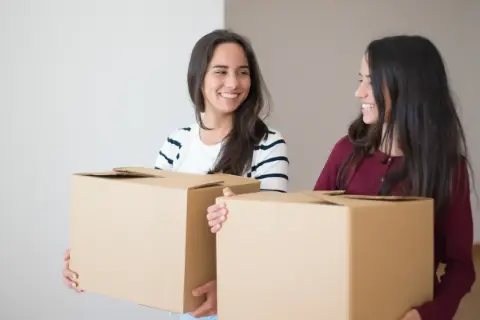 Due amiche sorridenti trasportano scatoloni, pronte per il precetto rilascio immobile prima della scadenza.