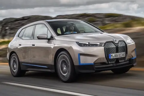 Złoty BMW iX jedzie po drodze, otoczony skalistym krajobrazem.