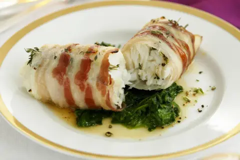 Zwei Fischröllchen, in Speck gewickelt, auf Spinatbett. Ein festliches Gericht, perfekt für Fischgerichte an Weihnachten.