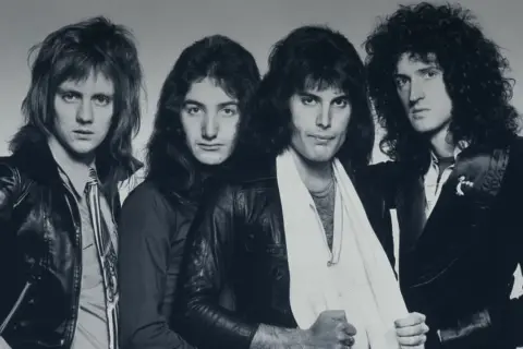 Die Mitglieder von Queen posieren für ein Schwarz-Weiß-Foto. Von links nach rechts: Roger Taylor, John Deacon, Freddie Mercury und Brian May.